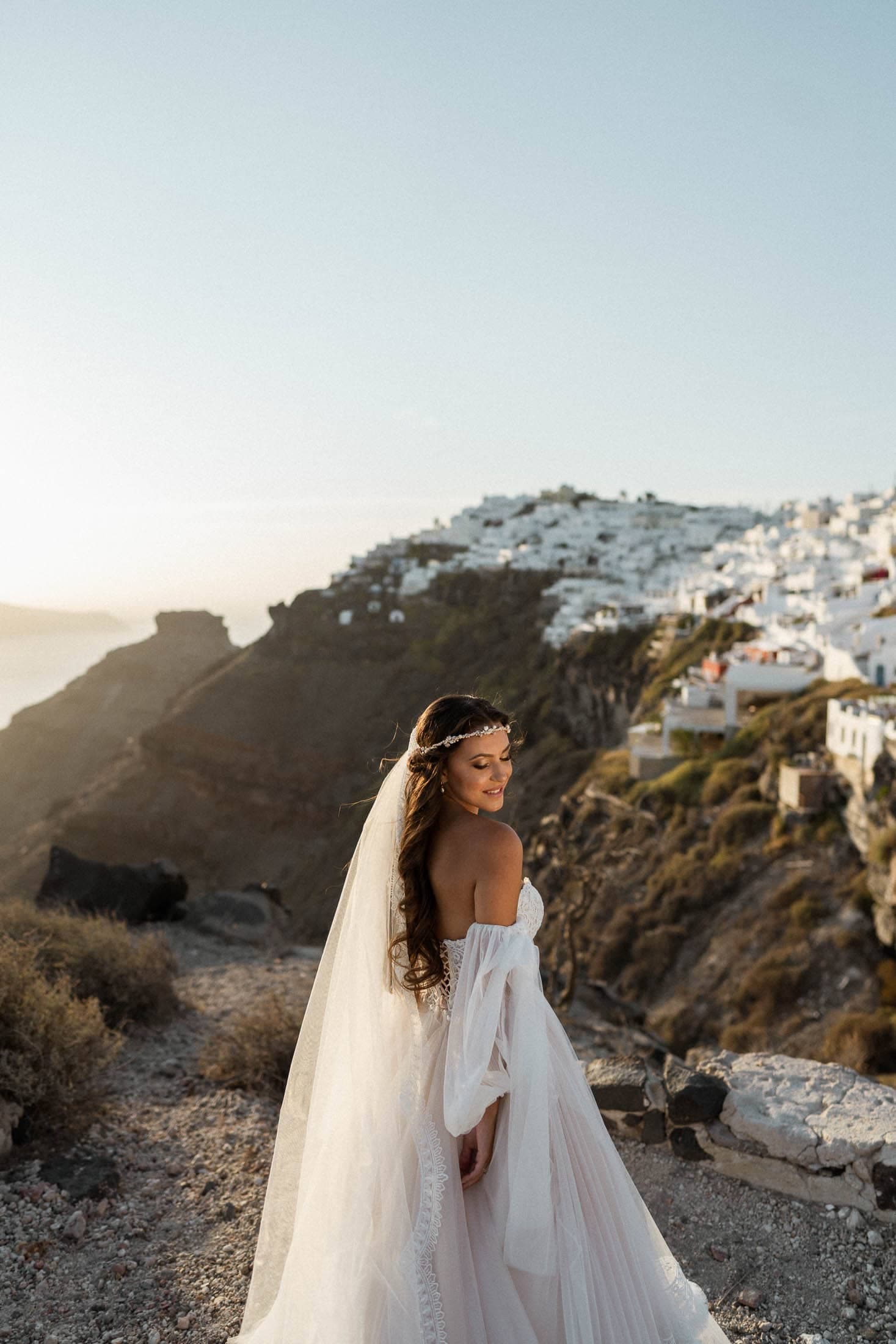 Bride posing in Imerovigli during sunset with white houses and Skaros rock in the background.