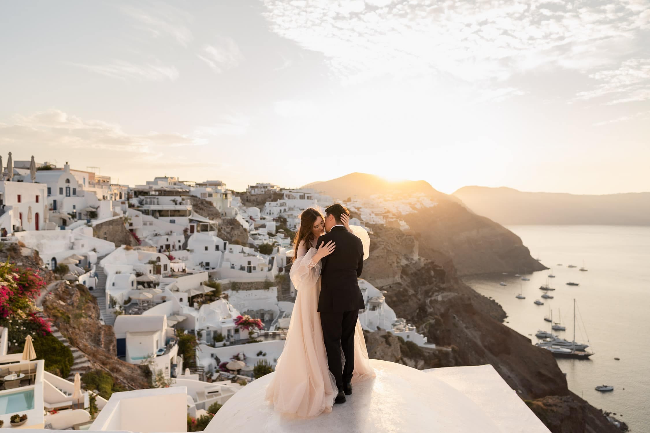 Wedding couple possing at the top of a dome in Oia, Santorini during a vivid sunset.