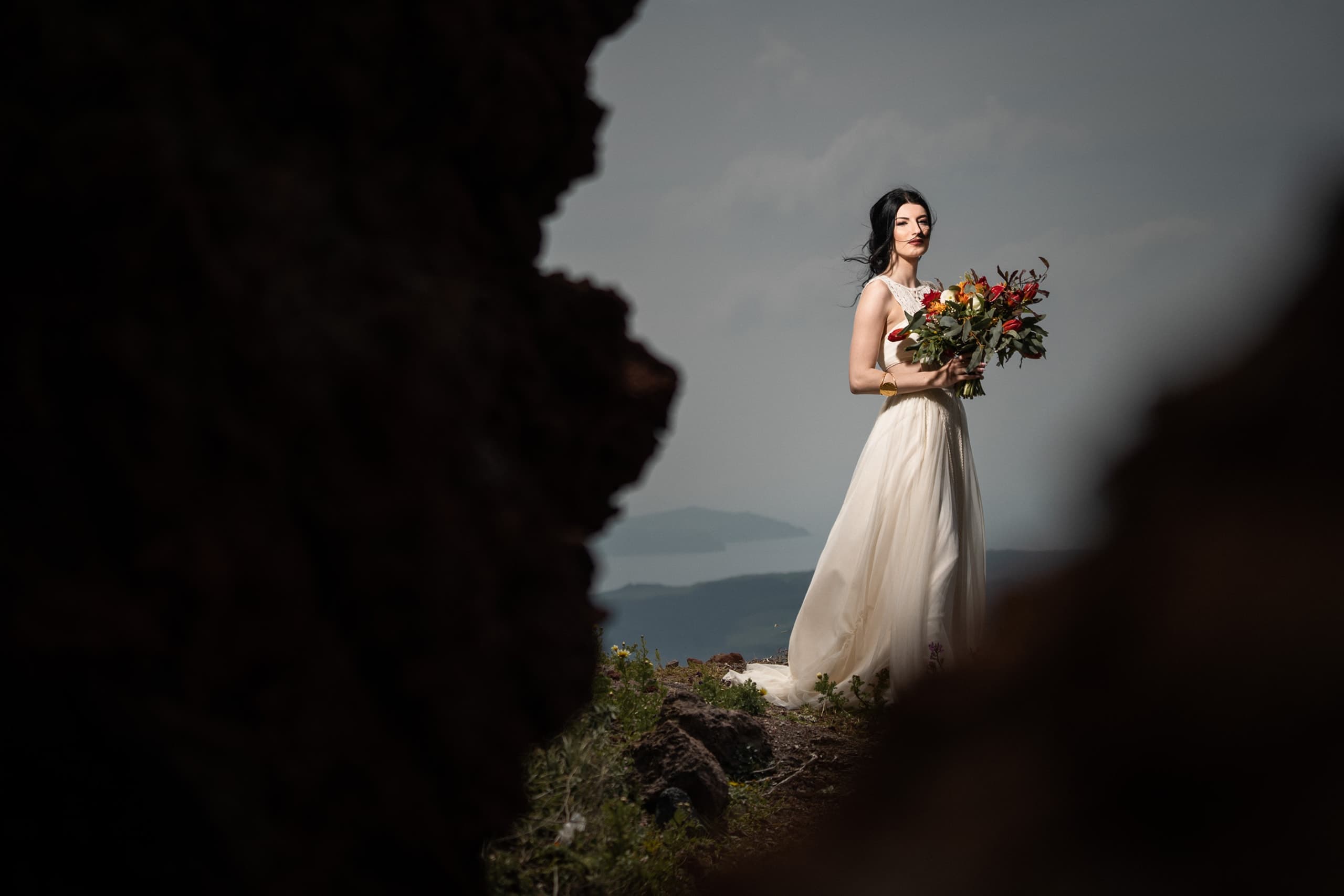 Bridal portrait in Skaros rock. Bride wearing a boho dreess holding her bouquet in Santorini.