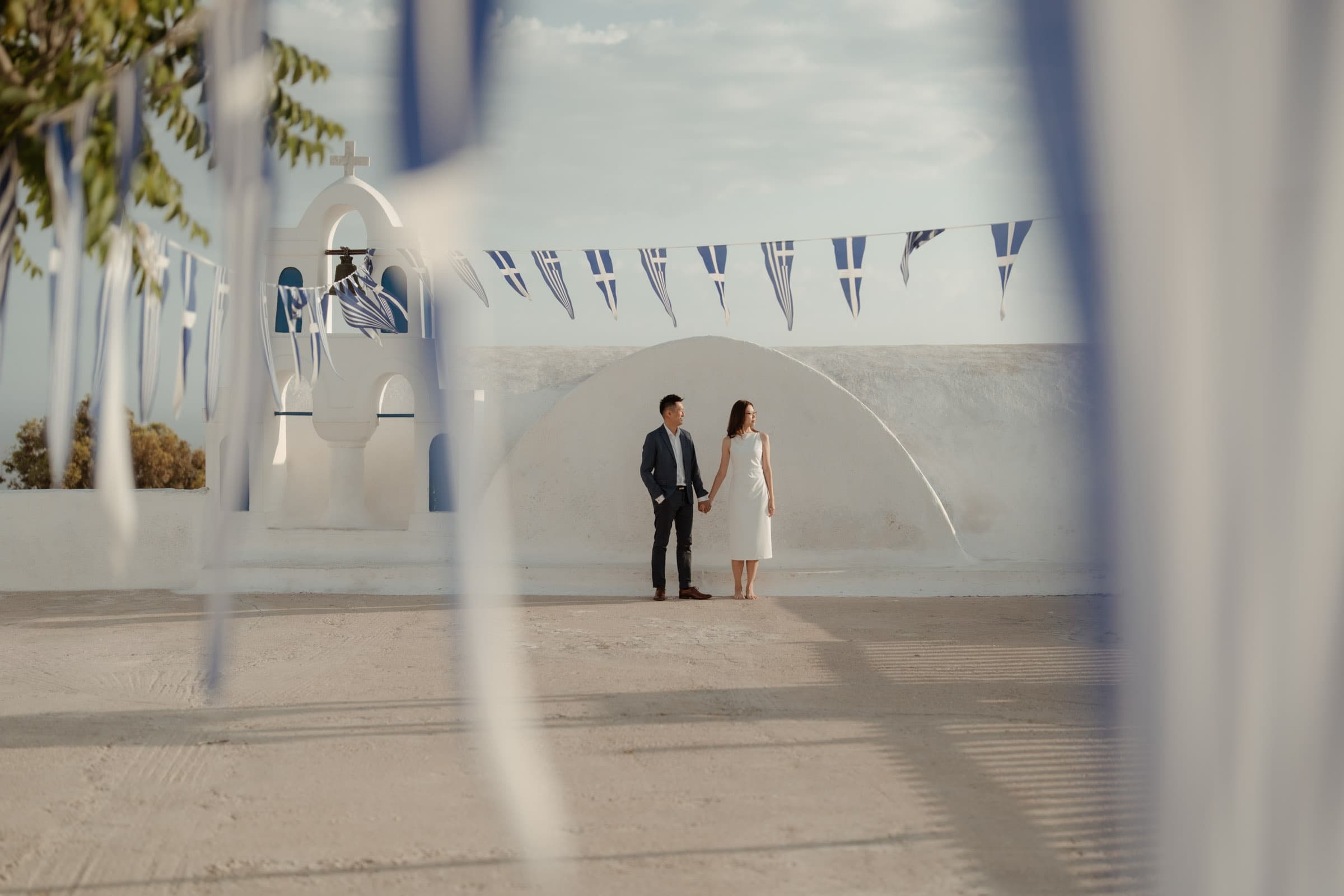 Couple posing in Oia among Greek flags, enjoying their private photoshoot.