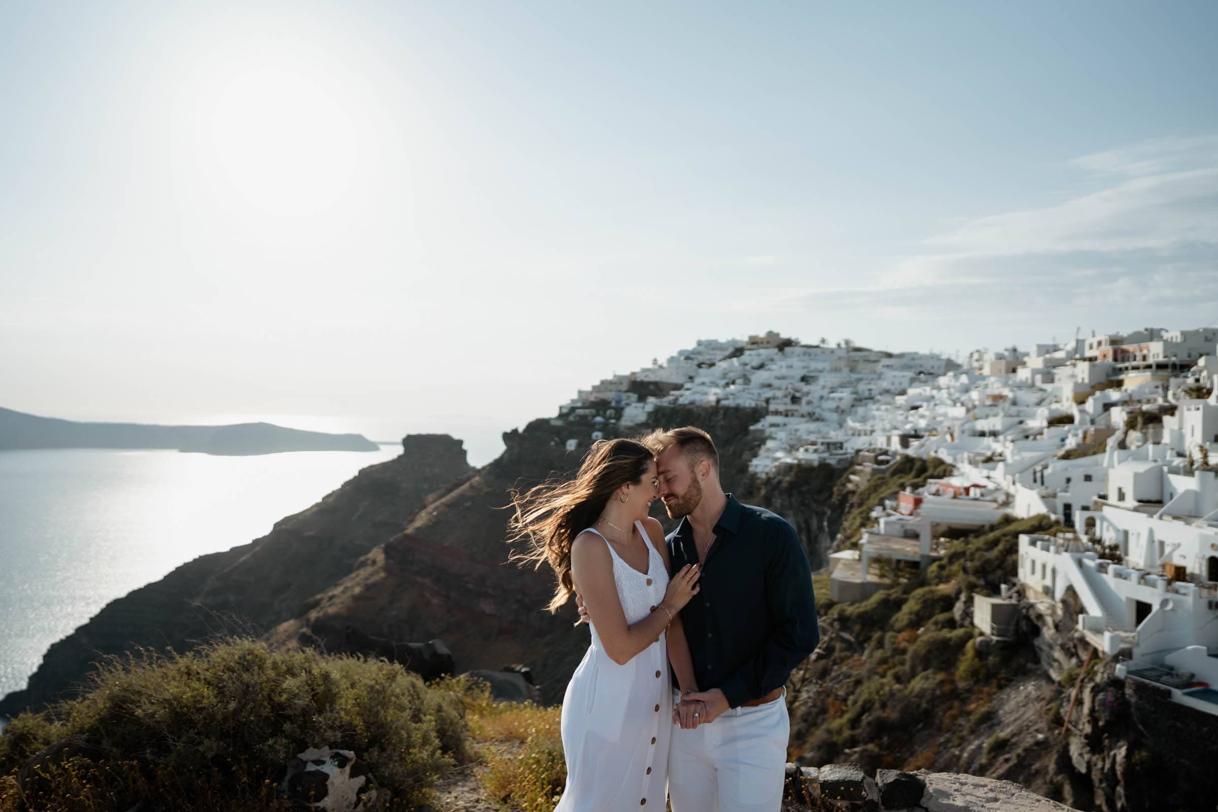 Couple posing in Imerovigli, enjoying their private photoshoot. White houses and blue domes in the background.