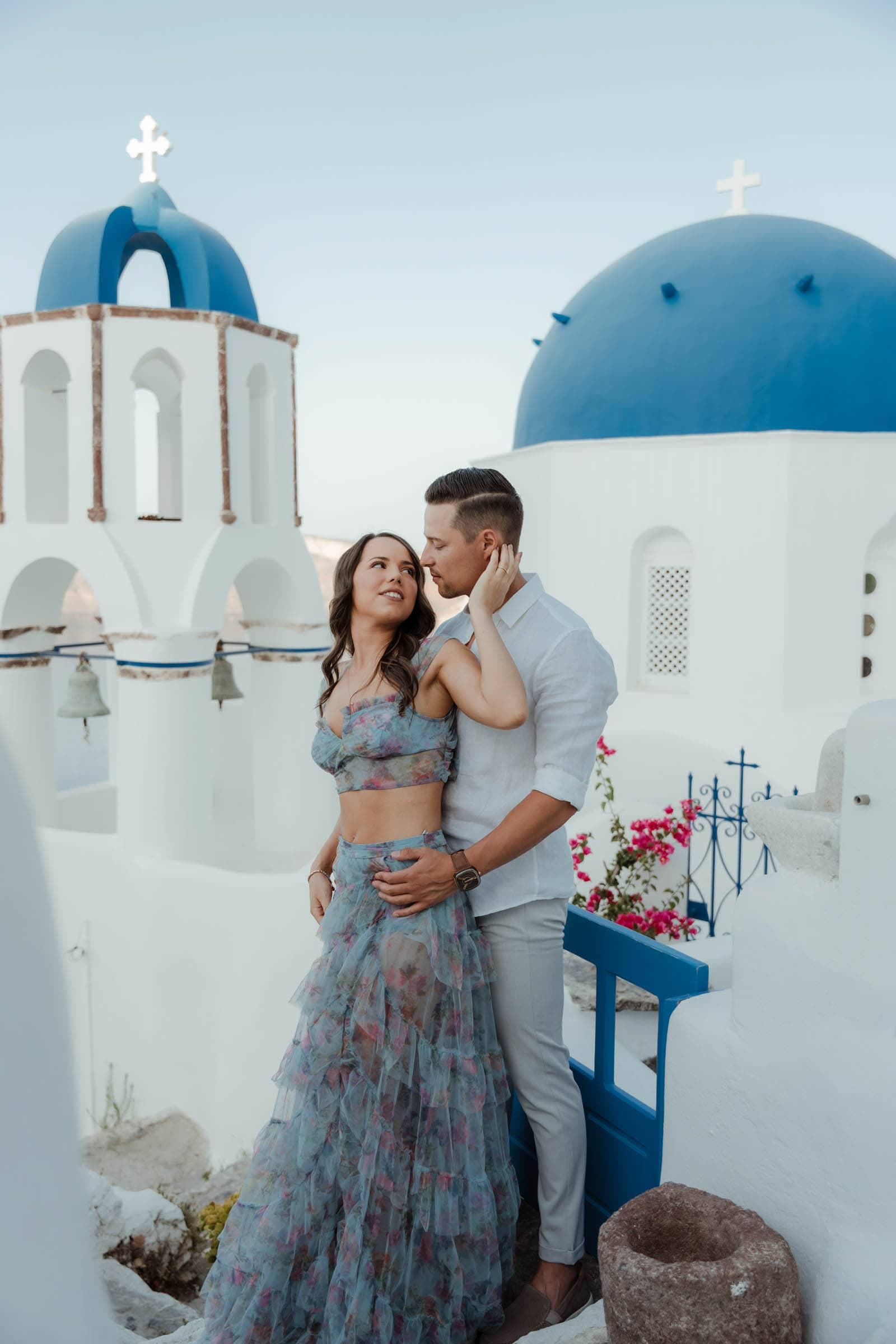 Couple posing in front of a blue dome in Oia. They are taking pictures after he proposed to her.
